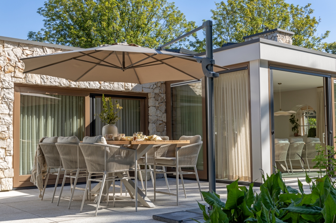 Große Garten Essgruppe mit Polyrattan-Stühlen und Sonnenschirm auf einer modernen Terrasse vor einem Haus mit Glasfront.